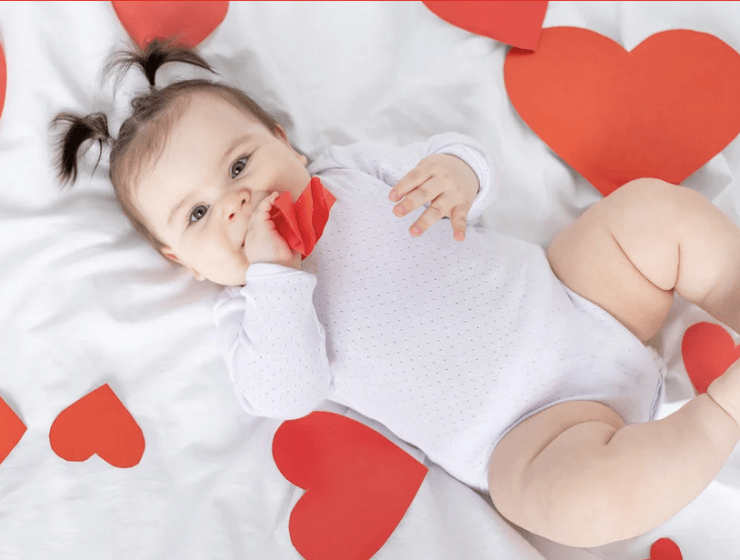Baby in white onesie laying on a white background surrounded by hearts.